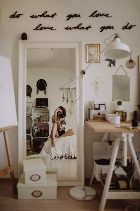 Frau fotografiert sich selbst und Zimmer mit weißer Einrichtung im Spiegel